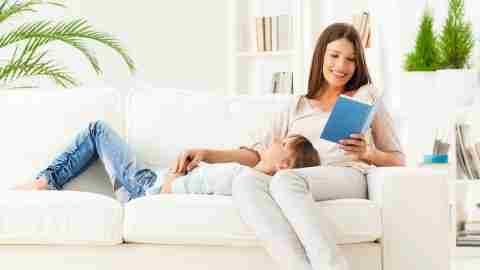 A mom reads a book about executive function to her daughter laying in her lap on the couch