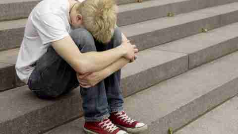 A sad boy with ADHD sits on the stairs hiding his face