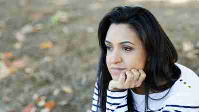 A woman with ADHD sits on the ground with her hand on her chin and looks thoughtfully into the distance