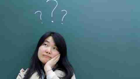 Asian women leans against a chalkboard with question marks above her head wondering, Do I have ADHD? She can take the free female adhd test to find out.