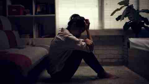 A woman with depression sits in a darkened room.