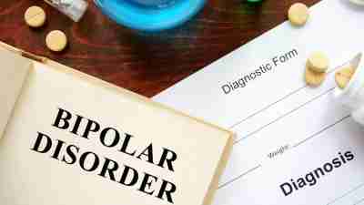 Book about bipolar disorder with diagnostic form next to it surrounded by different types of medication