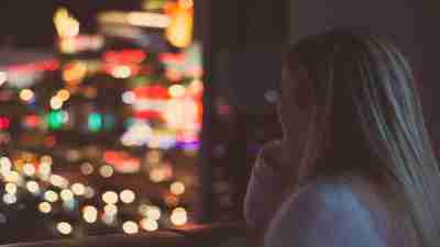 Girl with ADHD and depression stares out from apartment onto city street at night