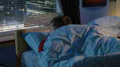 Medium shot of a boy looking out window while lying in bed and trying to fall asleep