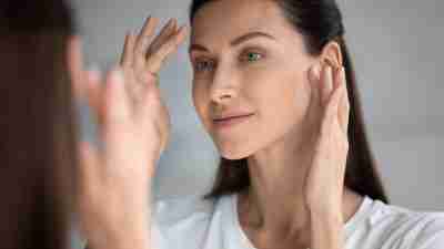 Close up woman looking in mirror, touching face in EFT tapping