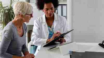 A female doctor sits at her desk and chats to an elderly female patient while looking at her test results