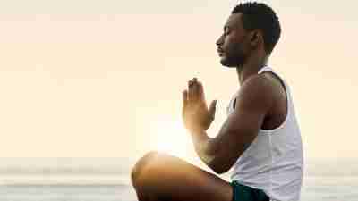 Resiliency: Adult man sits on beach, meditating in front of sunset.