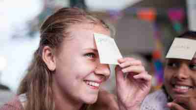 Family members playing the guessing game 'who am I?' Notes stuck to their foreheads, with animal names, smiling. One girl guessed correctly.