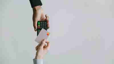 Hands holding a credit card and a payment terminal, illustrating a transaction. ADHD overspending advice.