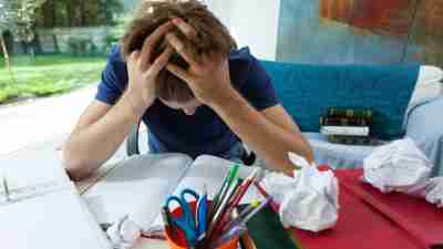 ADHD student with head in hands surrounded by books and paper overwhelmed by disorganization in room