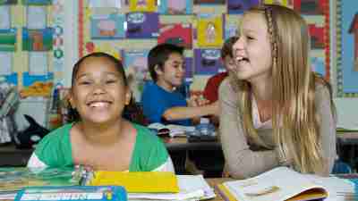 Two schoolgirls with ADHD sitting at desk and laughing