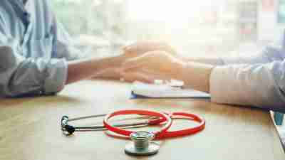 A doctor holds a patient's hand while meeting to titrate medication.