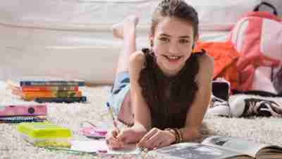 Girl with ADHD doing homework on carpet with books.